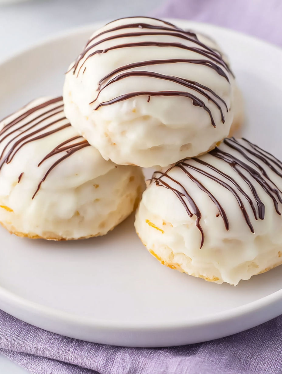 Three white donuts with chocolate stripes on a plate.