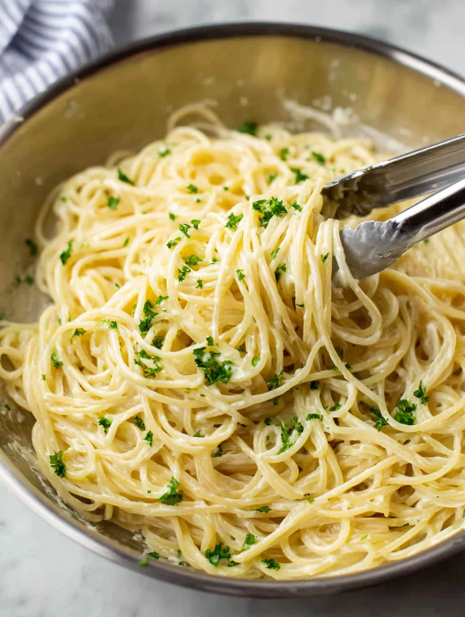A spoon is in a bowl of pasta with Parmesan cheese and herbs.