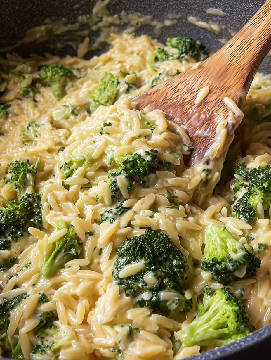 A wooden spoon is stirring a dish of pasta and broccoli.