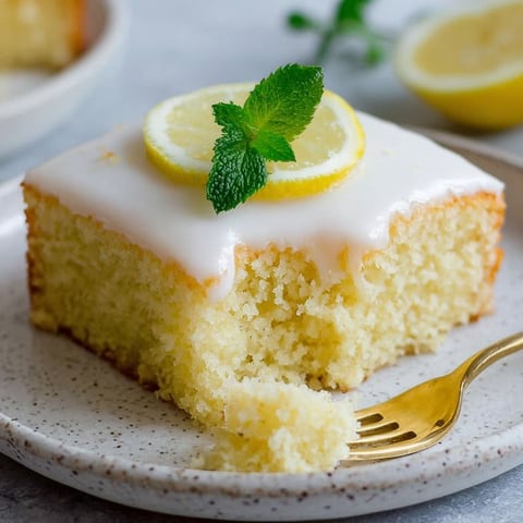 A slice of lemon cake with a green mint leaf on top.