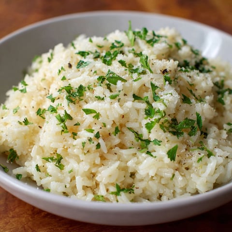 A bowl of rice with parmesan cheese and green herbs.