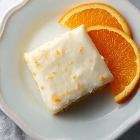 A slice of blonde orange brownies with a orange slice on the side.