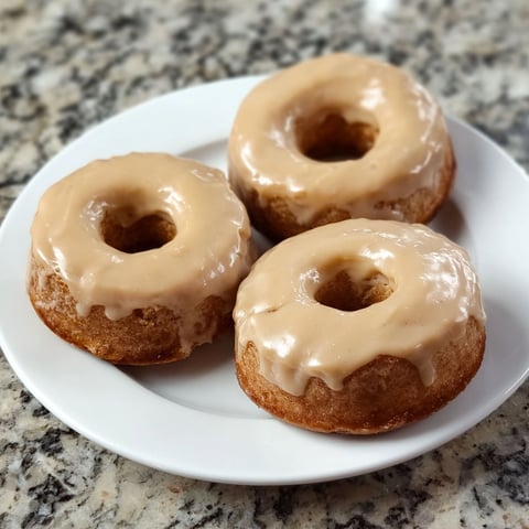 Three donuts with glaze on a plate.