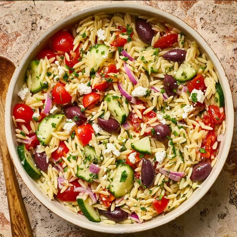 A bowl of pasta salad with tomatoes, cucumbers, olives, and feta cheese.