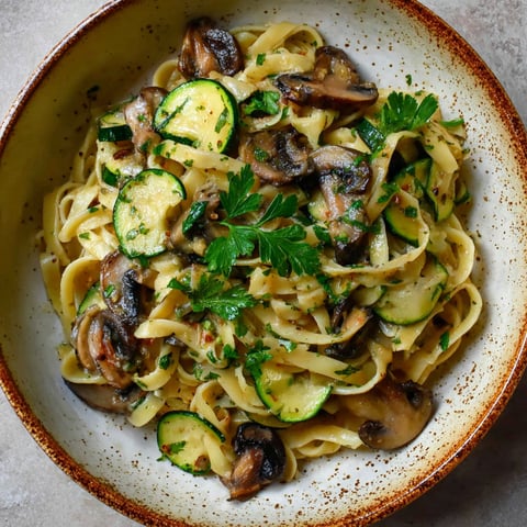A bowl of pasta with mushrooms and zucchini.