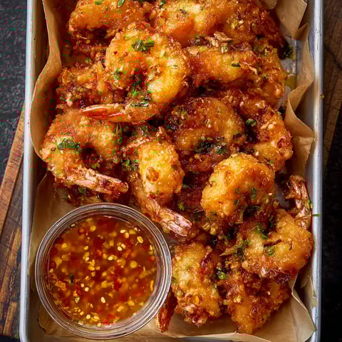 A container of fried shrimp with a dipping sauce.